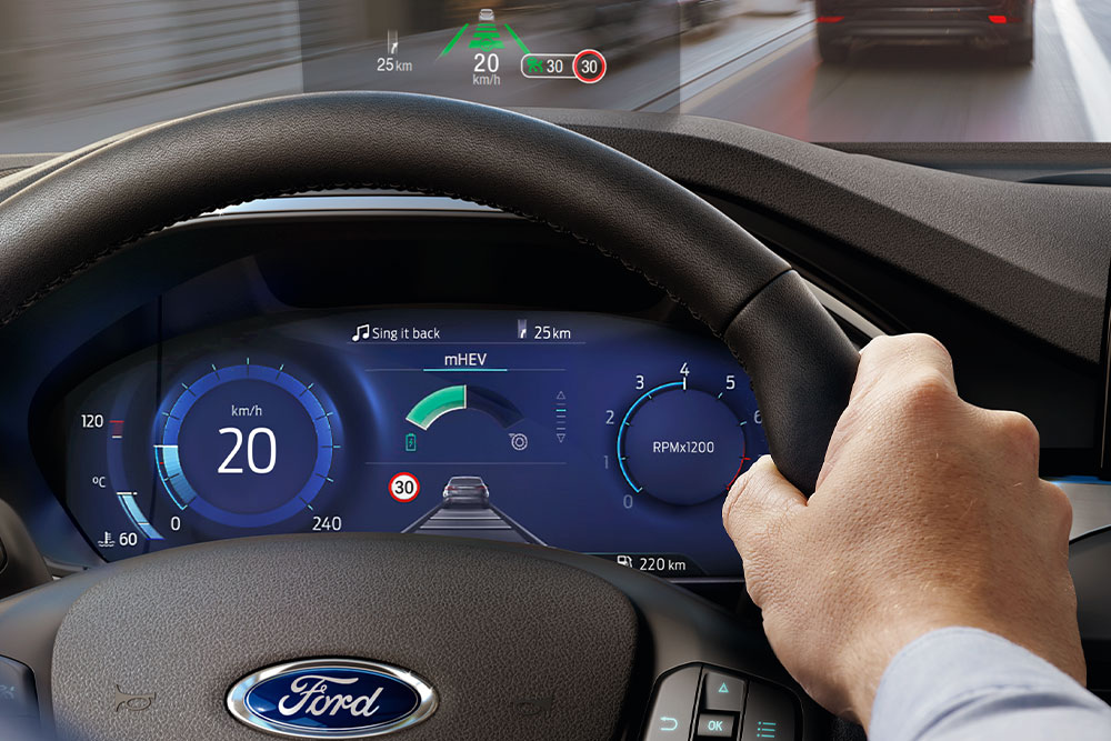 Imagen de una mano en el volante con un pequeño monitor sobre el panel de control.